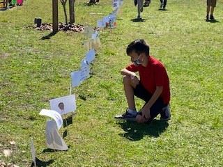 A young boy kneeling on the grass looking at student artwork. 