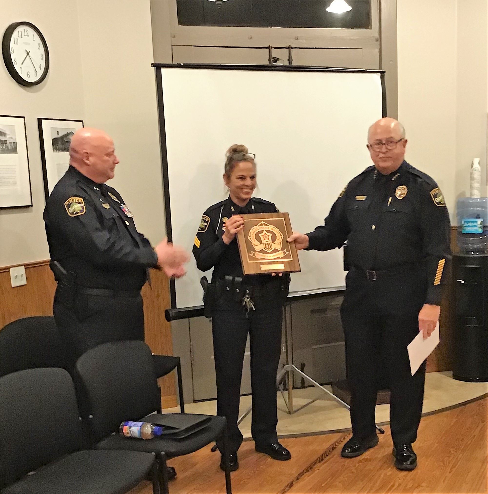 Sergeant Campbell holds plaque while Chief Thomas stands to her right and helps to hold plaque. Depu