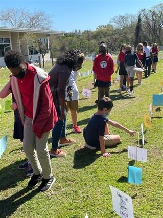 A female teacher and several students admiring student artwork outside for the Harmony Walk. 